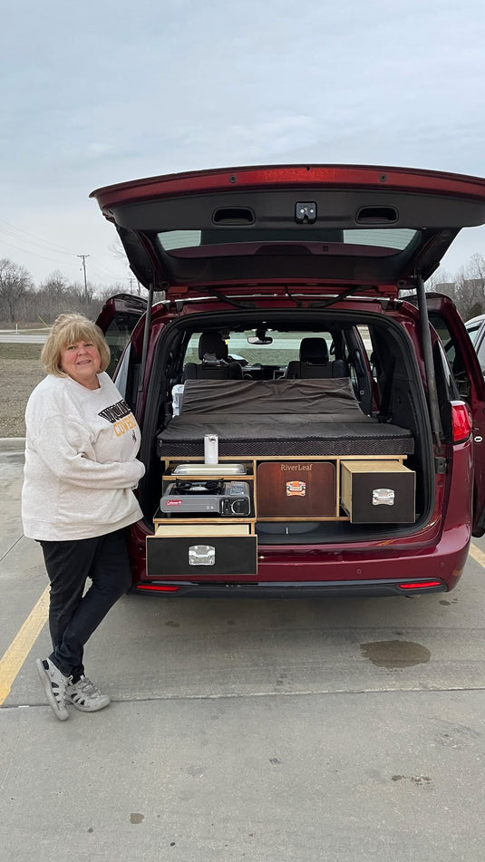 Woman standing next to a red Chrysler pacifica car with an open trunk displaying camping conversion